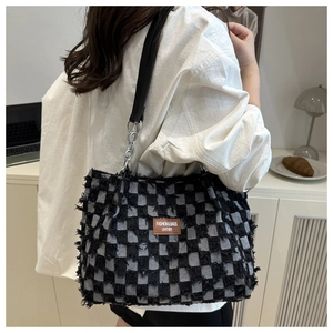 Detail of checkered tote bag with fringe edges and metal chain strap in office setting
