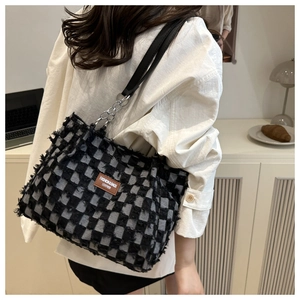 Detail of checkered denim bucket bag with frayed edges and brown leather fashion tag