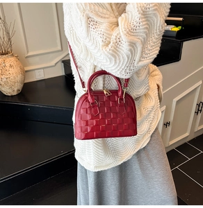 Detail of red embossed shell bag with gold hardware worn by a model in a knit sweater