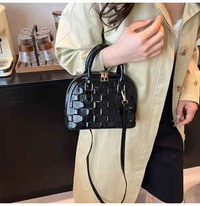 Detail of a black glossy shell-shaped handbag featuring textured grid patterns and gold hardware