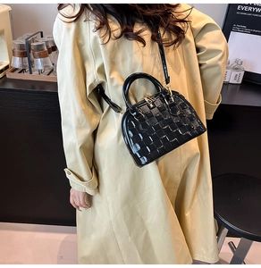 Detail of glossy black shell bag with quilted texture worn by model in beige trench coat