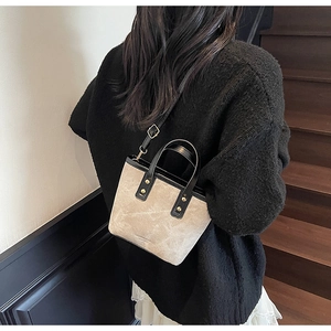 Detail of a mini beige canvas bucket bag with black leather trim and gold rivet accents