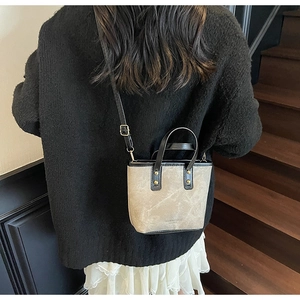Detail of khaki bucket bag with black leather trim and elegant gold hardware accents