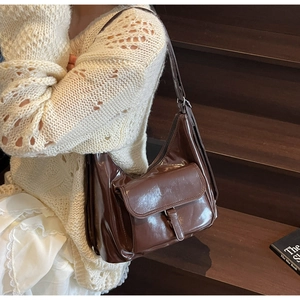 Detail of dark brown glossy shoulder bag showing front flap pocket and buckle closure