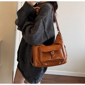 Close-up of caramel patent leather hobo bag with metal buckle detail on a model