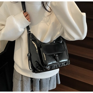 Detail view of black glossy tote bag with flap pocket and adjustable strap worn on person