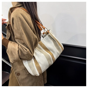 Detail of striped canvas tote bag with brown leather handles and metal hardware