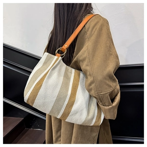 Detail of striped canvas tote bag with leather shoulder strap worn over a wool coat