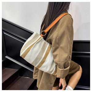 Detail of striped canvas tote bag featuring brown leather straps and gold metal rings
