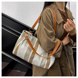 Macro detail of canvas stripe tote bag featuring brown leather straps and metal rings