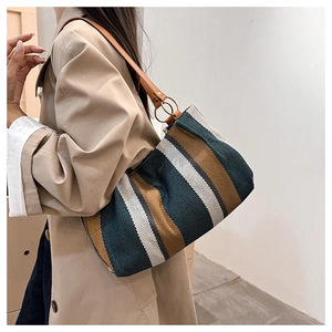 Detail of canvas tote bag featuring tricolor stripes and brown leather strap with metal ring