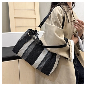 Close-up of striped canvas tote bag showing black leather straps and gold metal rings