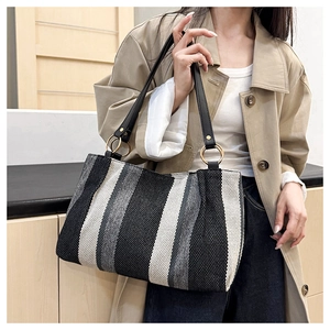 Detail of striped canvas tote bag showing black leather straps and gold metal rings