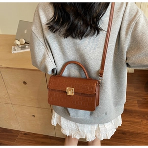 Detail of dark brown crocodile embossed crossbody bag with vintage gold metal lock closure