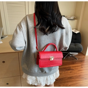 Detail of red crocodile texture crossbody bag with gold square buckle worn by a model
