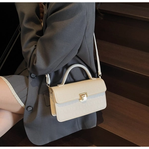 Detail of off-white crocodile pattern handbag with golden metal twist lock and top handle