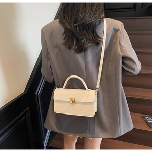 Detailed view of crocodile embossed leather texture and gold twist lock on cream handbag