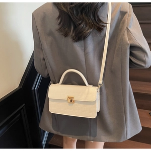 Sac bandoulière motif crocodile crème porté par un mannequin dans un escalier