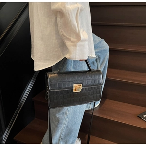 Détail d'un sac à bandoulière noir à texture crocodile avec fermoir en métal doré