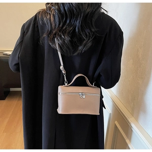 Dettaglio borsa a tracolla in pelle beige su blazer nero con trama e cinturino in vista