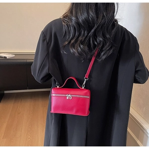 Dettaglio di una borsa a tracolla in pelle rossa indossata su un blazer nero per l'autunno