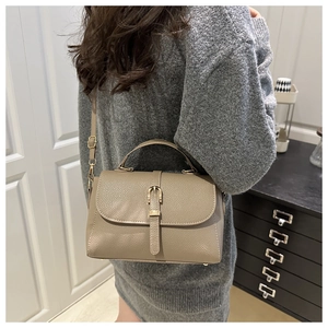 Brown lychee leather crossbody bag with gold buckle detail shown on model in room