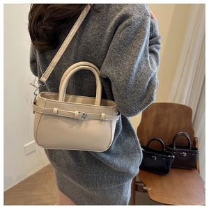 Detailed view of beige minimalist handbag with strap showing size on the model
