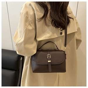 Detail view of coffee-colored crossbody bag with golden buckle and textured leather