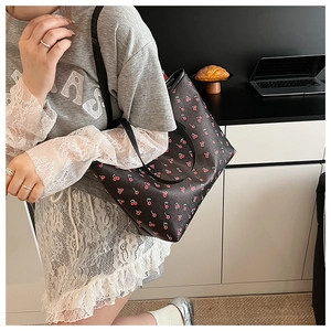 Close-up of black tote bag with red cherry print worn by a model in casual setting