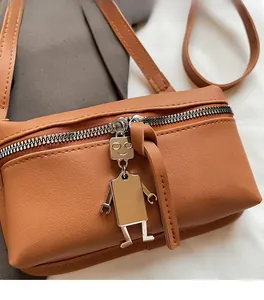 Detail of caramel brown crossbody bag showing soft leather texture and silver robot charm