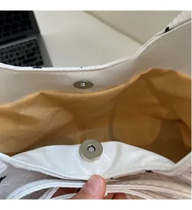 Détail de boucle magnétique argentée sur sac blanc avec doublure en satin jaune et fini poli