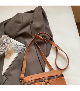 Detail view of brown leather crossbody bag with adjustable strap and silver metal zipper