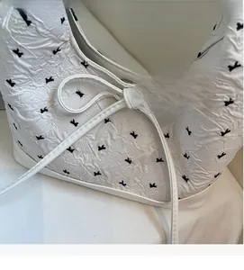 Détail du sac bandoulière plissé blanc avec imprimé ruban noir et nœud décoratif fin