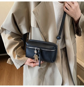 Detail of black crossbody box bag with silver robot pendant on a khakis coat