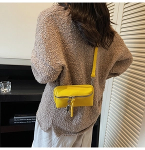 Detail of yellow crossbody bag featuring a silver metal robot pendant and zip closure
