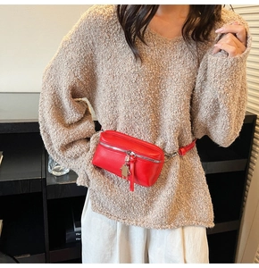 Detailed view of red mini leather belt bag with silver zipper and charm on sweater