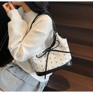 Détail du sac en tissu texturé blanc avec broderie d'étoiles noires et grand nœud en soie