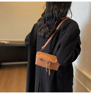 Detail view of a tan leather square crossbody bag with silver zipper and long fringe tassel