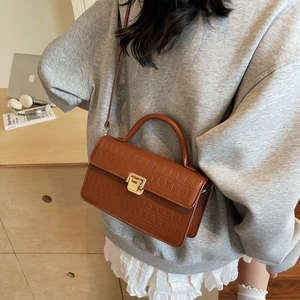 Sac à bandoulière marron effet crocodile avec boucle dorée porté par un modèle