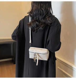 Detail of off-white crossbody bag with unique silver robot charm on black coat