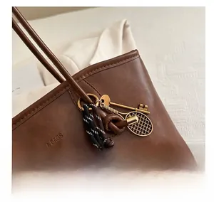 Détail du sac cabas en cuir marron avec breloques raquette de tennis dorée