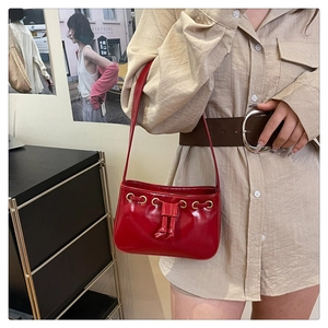 Detail of red patent leather underarm bag featuring drawstring and golden metal rings
