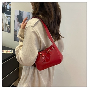 Detail of red patent leather underarm bag with drawstring design and gold eyelets