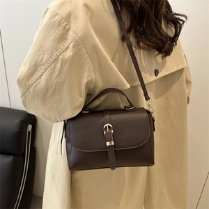 Deep brown textured leather handbag with gold buckle shown on a beige trench coat
