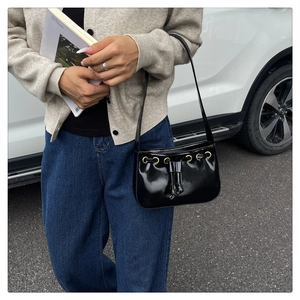Close-up of black glossy patent leather shoulder bag with gold ring and bow detail