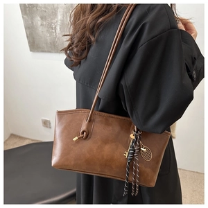 Détail du sac cabas en cuir marron avec breloques en métal et décoration de glands tissés