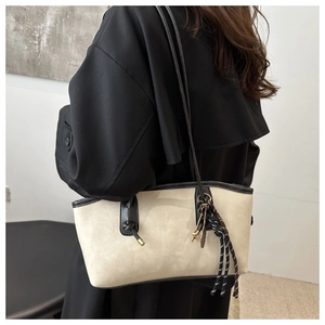Détail d'un sac cabas beige avec des anses noires et un charme tressé texturé