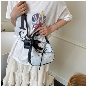 Détail du sac blanc avec motifs de nœuds rouges, bordure noire et pendentif cœur