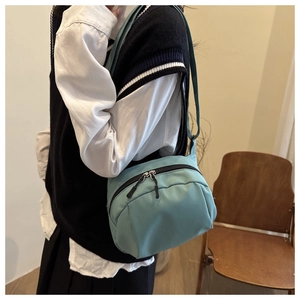 Detail view of light blue nylon crossbody bag with dual metal zippers and adjustable strap