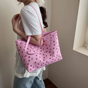 Pink tote bag with red cherry print and gold studs shown on a female model